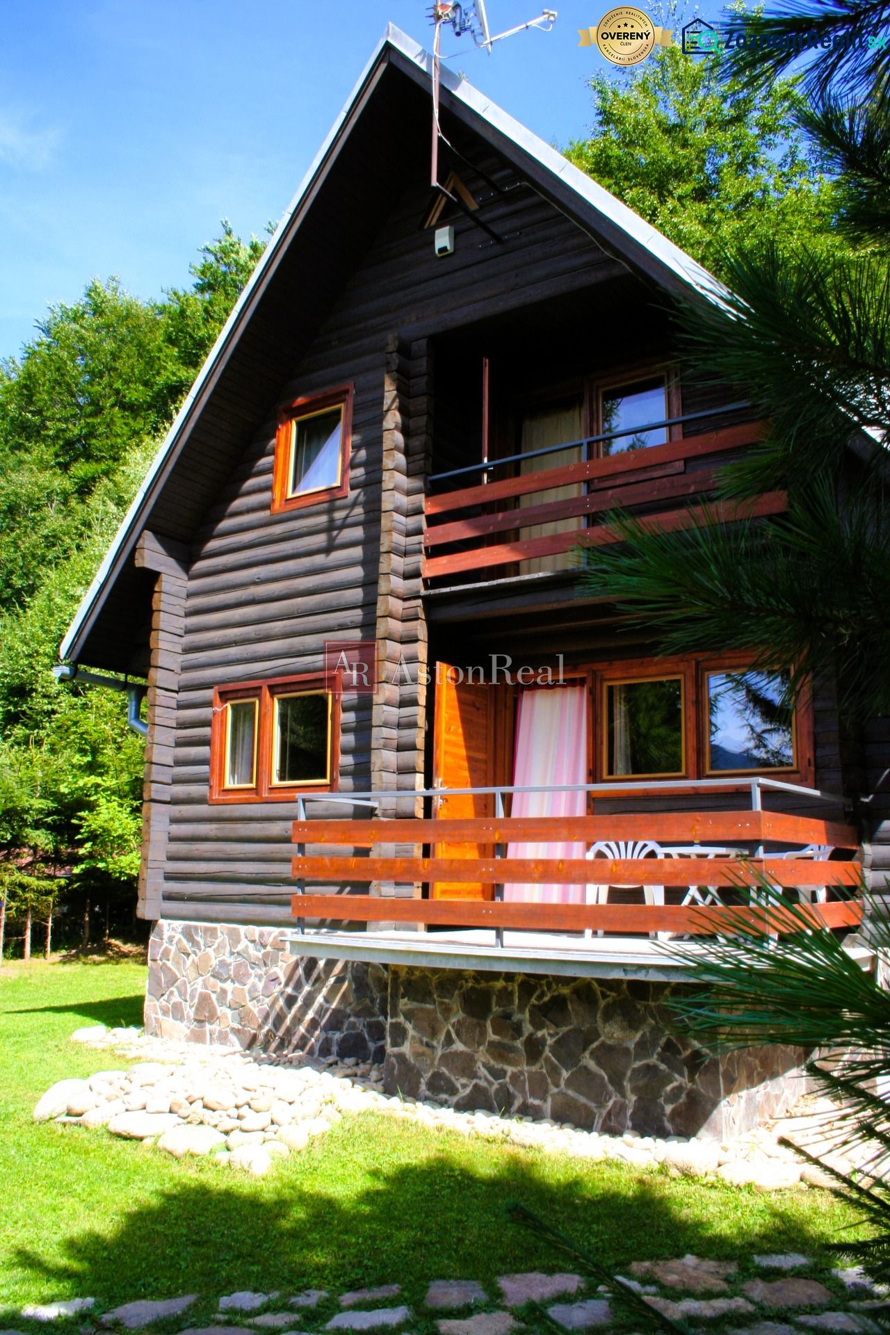 Holzhütte in Tále bei Brezno, umgeben von Grün mit einem Steinsockel und einer Terrasse.