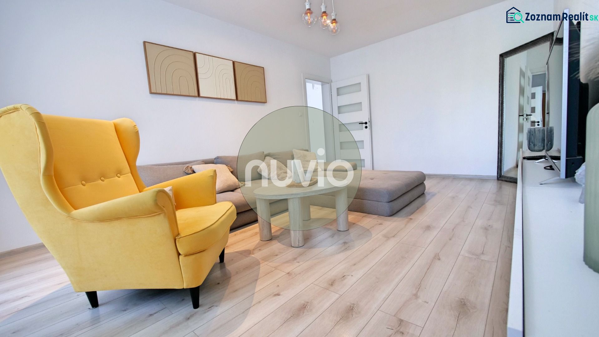 Wohnzimmer mit Holzboden, gelbem Sessel und Sofa in einer Zweizimmerwohnung.