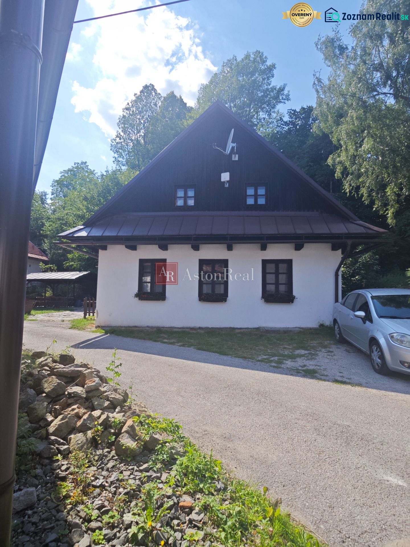 Ein Ferienhaus in Špania Dolina mit weißer Fassade und Satellitenschüssel, umgeben von Grün.