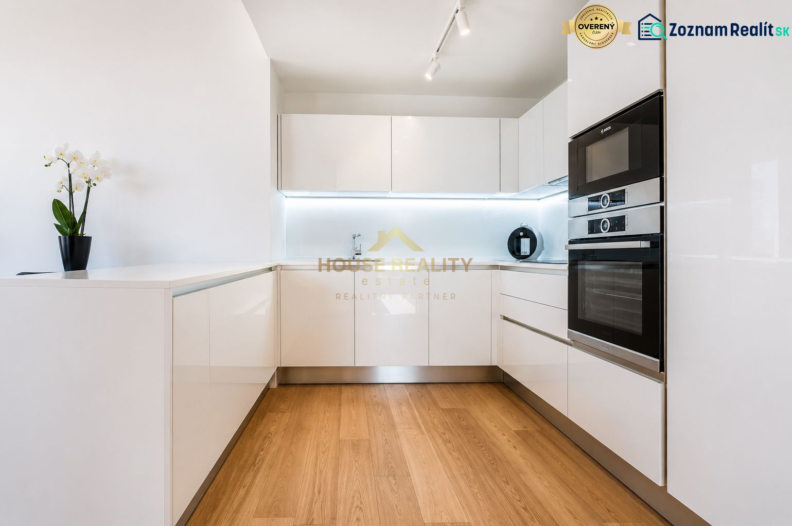 Küche in einer 3-Zimmer-Wohnung mit weißen Schränken und einem Boden in Holzoptik.