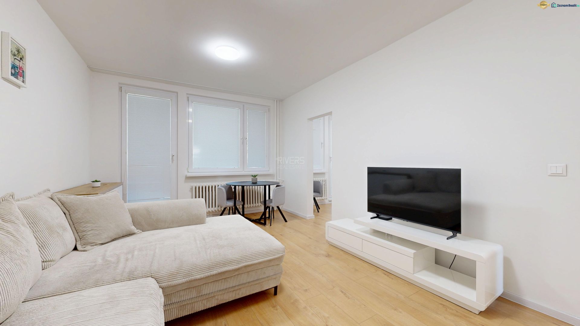 Wohnzimmer in einer 3-Zimmer-Wohnung mit Sofa, Fernseher und Holzboden.
