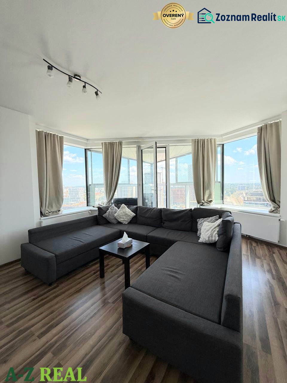 Geräumiger Wohnbereich mit dunklem Sofa und Boden in Holzoptik in einer 3-Zimmer-Wohnung.