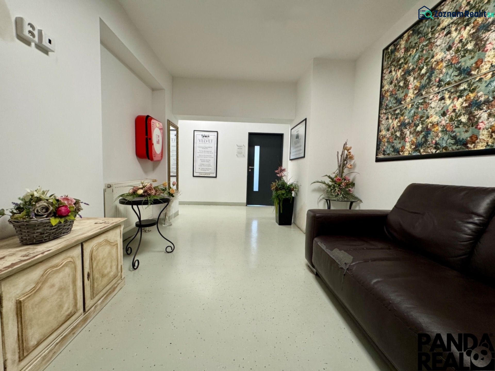 Empfangsbereich in Geschäftsräumen mit dunklem Sofa und Blumendekorationen.