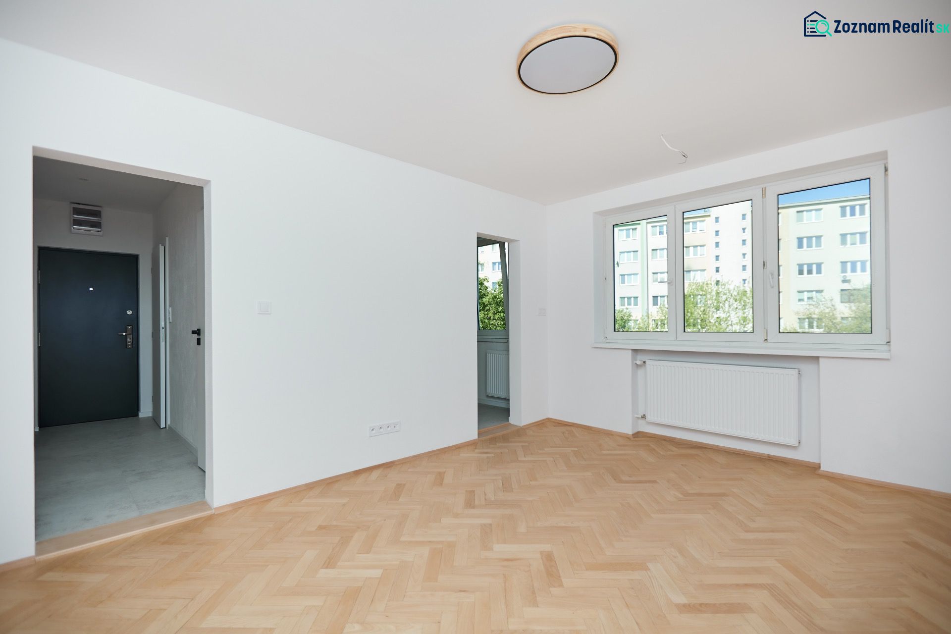 Eine Wohnung mit einem Holzboden, weißen Wänden und großen Fenstern.