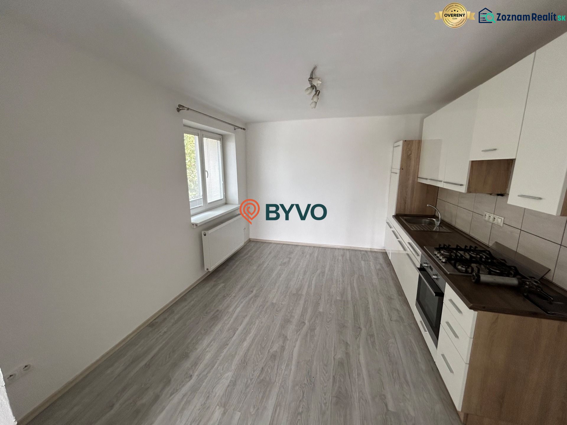 Küche mit weißer Küchenzeile in einer 3-Zimmer-Wohnung, Boden mit Holzdekor, großes Fenster.