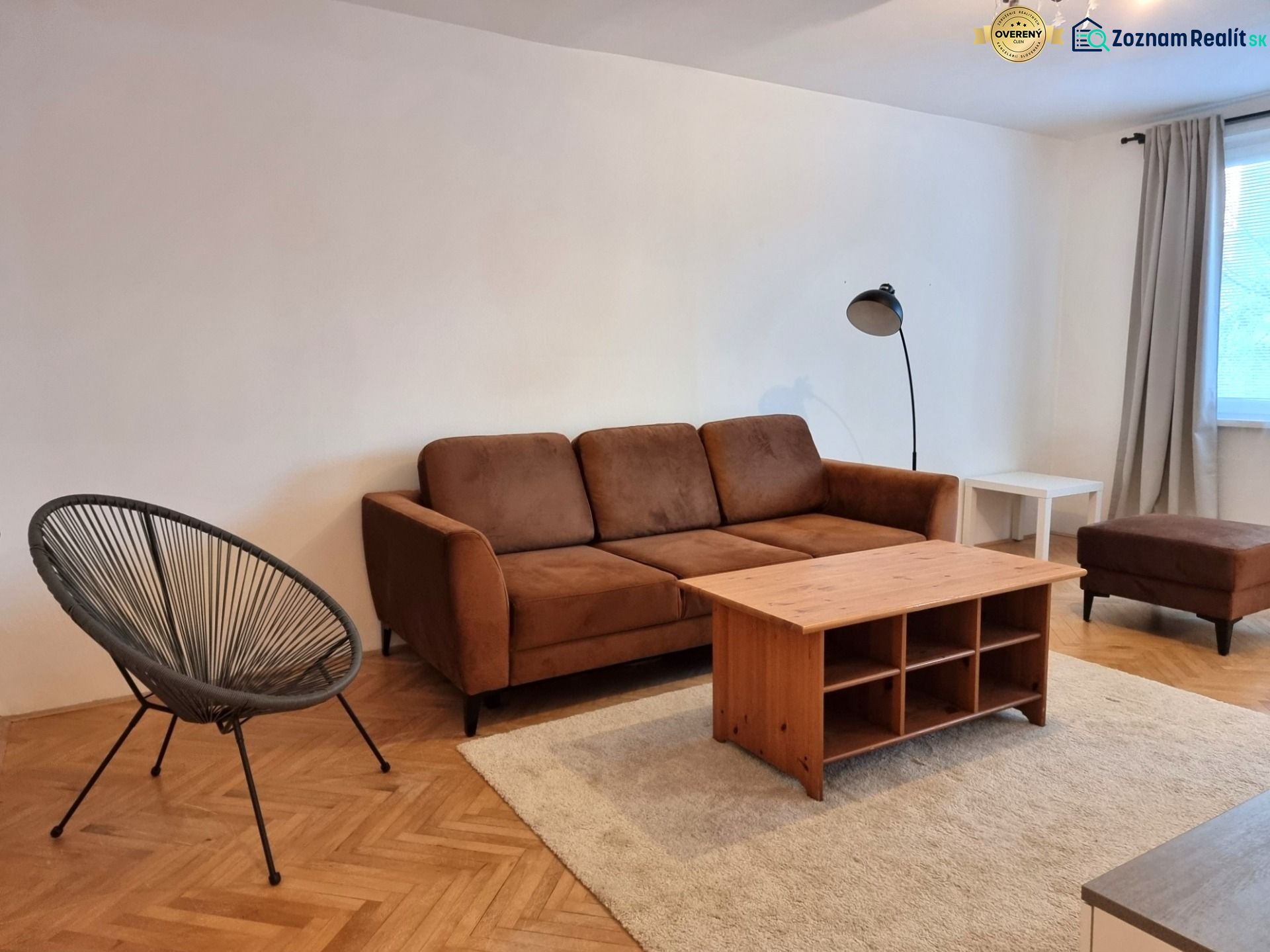 Wohnzimmer einer Zweizimmerwohnung mit braunem Sofa und Boden in Holzoptik.
