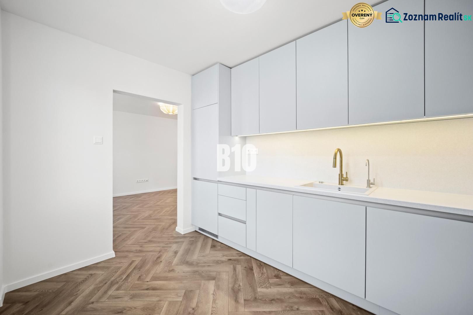 Küche in einer 3-Zimmer-Wohnung mit weißen Möbeln und einem Boden in Holzoptik.