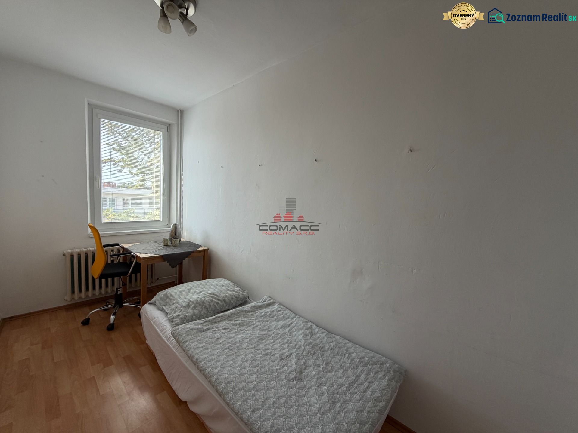Ein Zimmer in einer 3-Zimmer-Wohnung mit einem Bett, einem Tisch und einem Boden in Holzoptik.