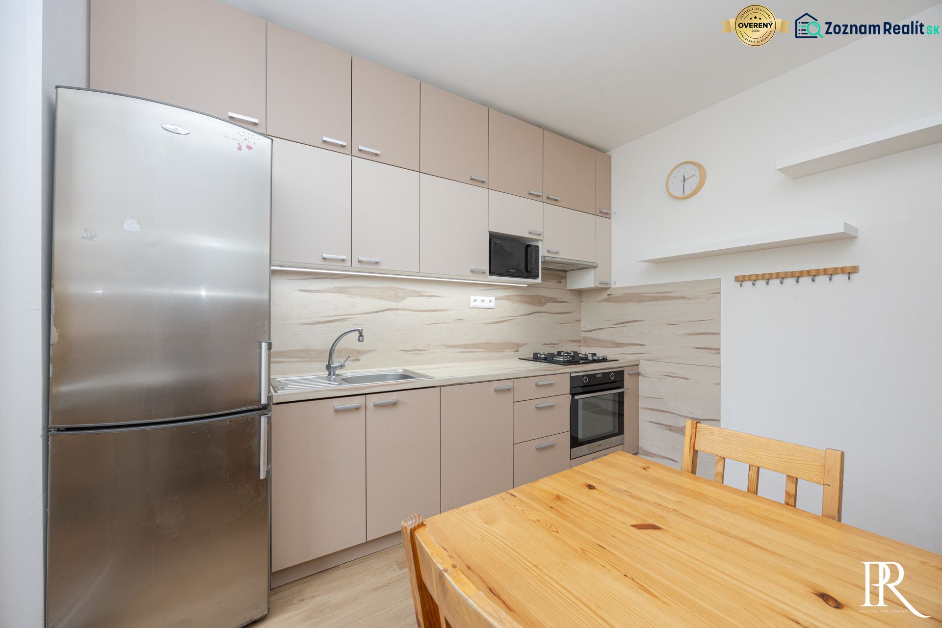 Küche in einer 3-Zimmer-Wohnung mit Kühlschrank, Holztisch und Küchenzeile.