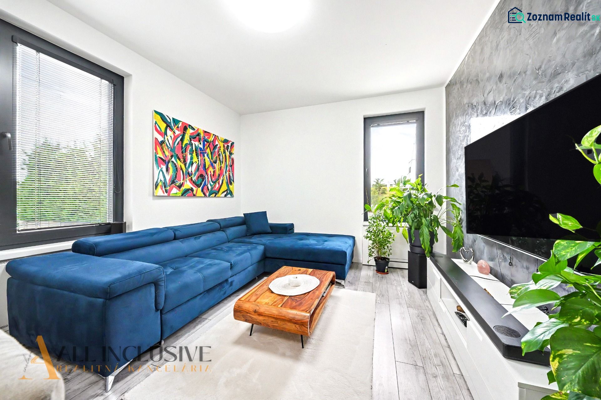 Wohnzimmer mit blauem Sofa und Pflanzen in einer 3-Zimmer-Wohnung, Boden mit Holzdekor.