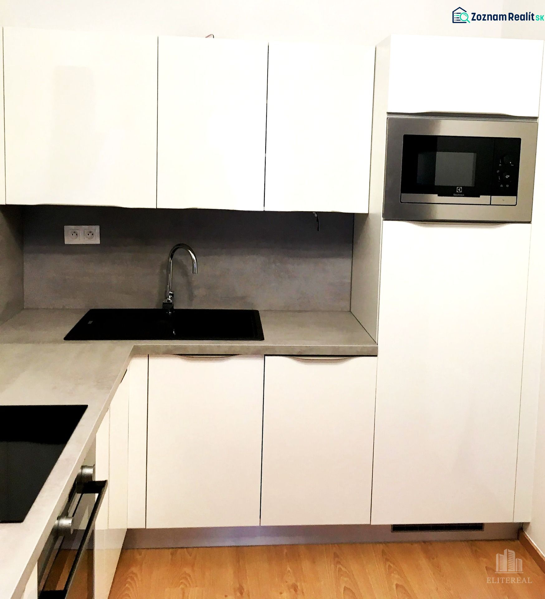 Weiße Küche mit Mikrowelle und eingebautem Spülbecken, 2-Zimmer-Wohnung, Boden mit Holzdekor.