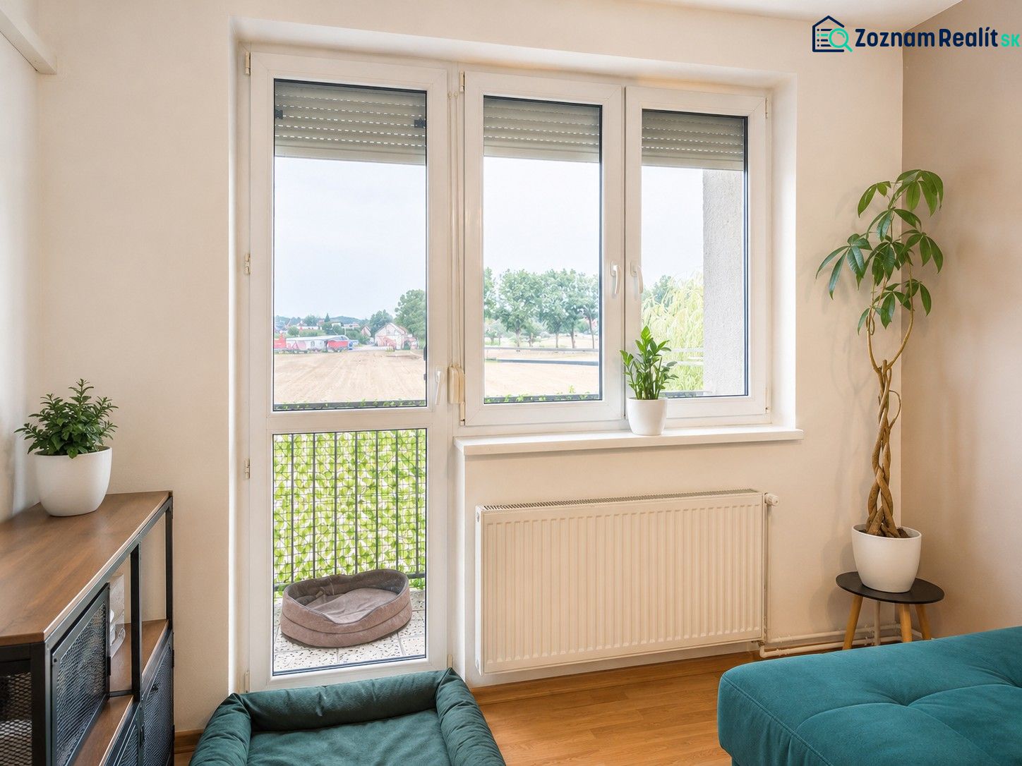Ein Zimmer in einer 4-Zimmer-Wohnung mit einem Fenster, Pflanzen und einem Boden in Holzoptik.