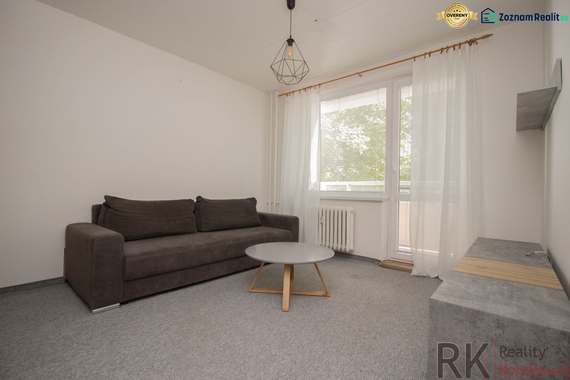 Wohnzimmer einer Einzimmerwohnung mit grauem Sofa, Tisch und Vorhängen.