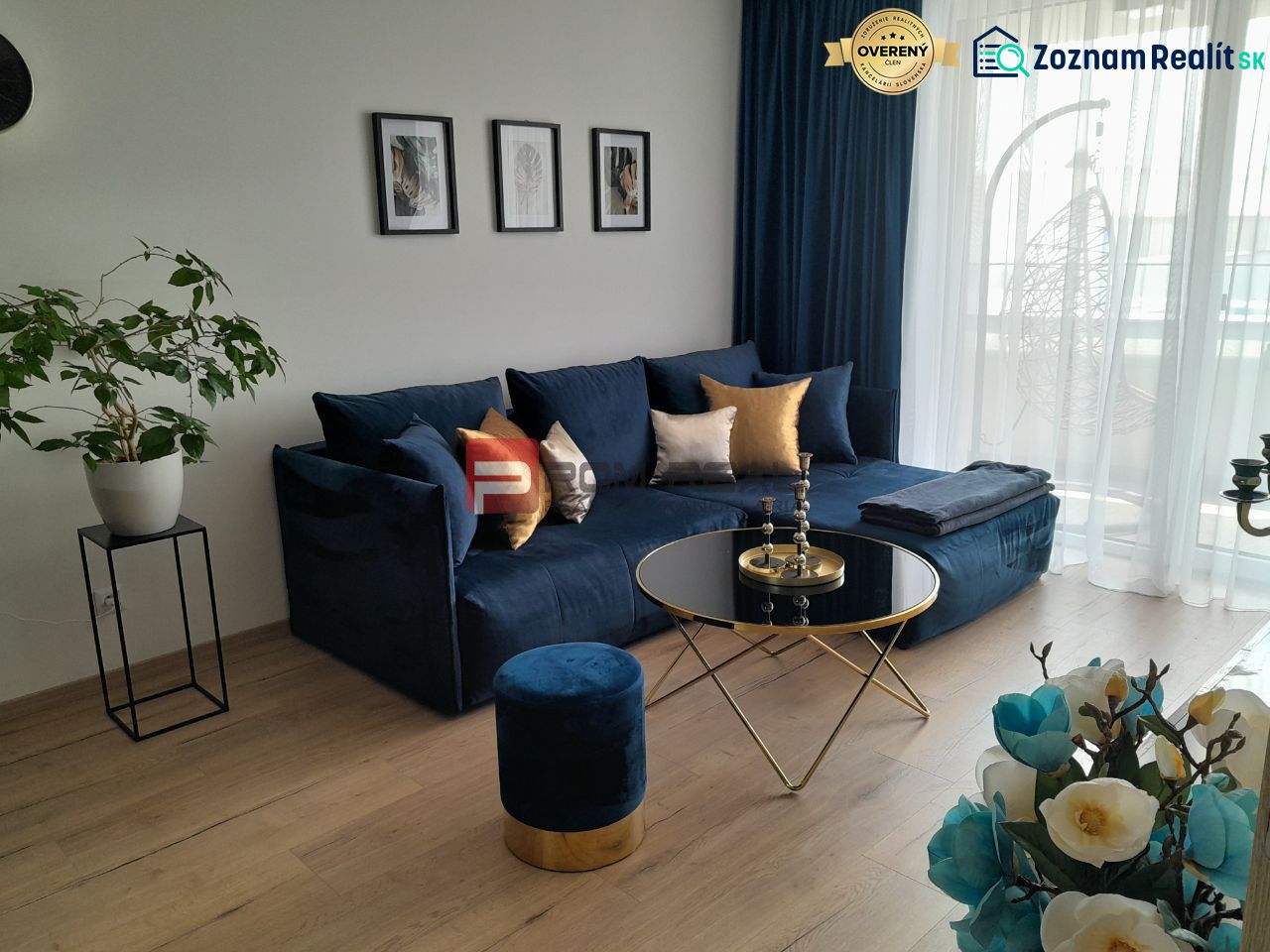 Wohnzimmer in einer Zweizimmerwohnung mit einem blauen Sofa, einem Boden in Holzoptik und Dekorationen.