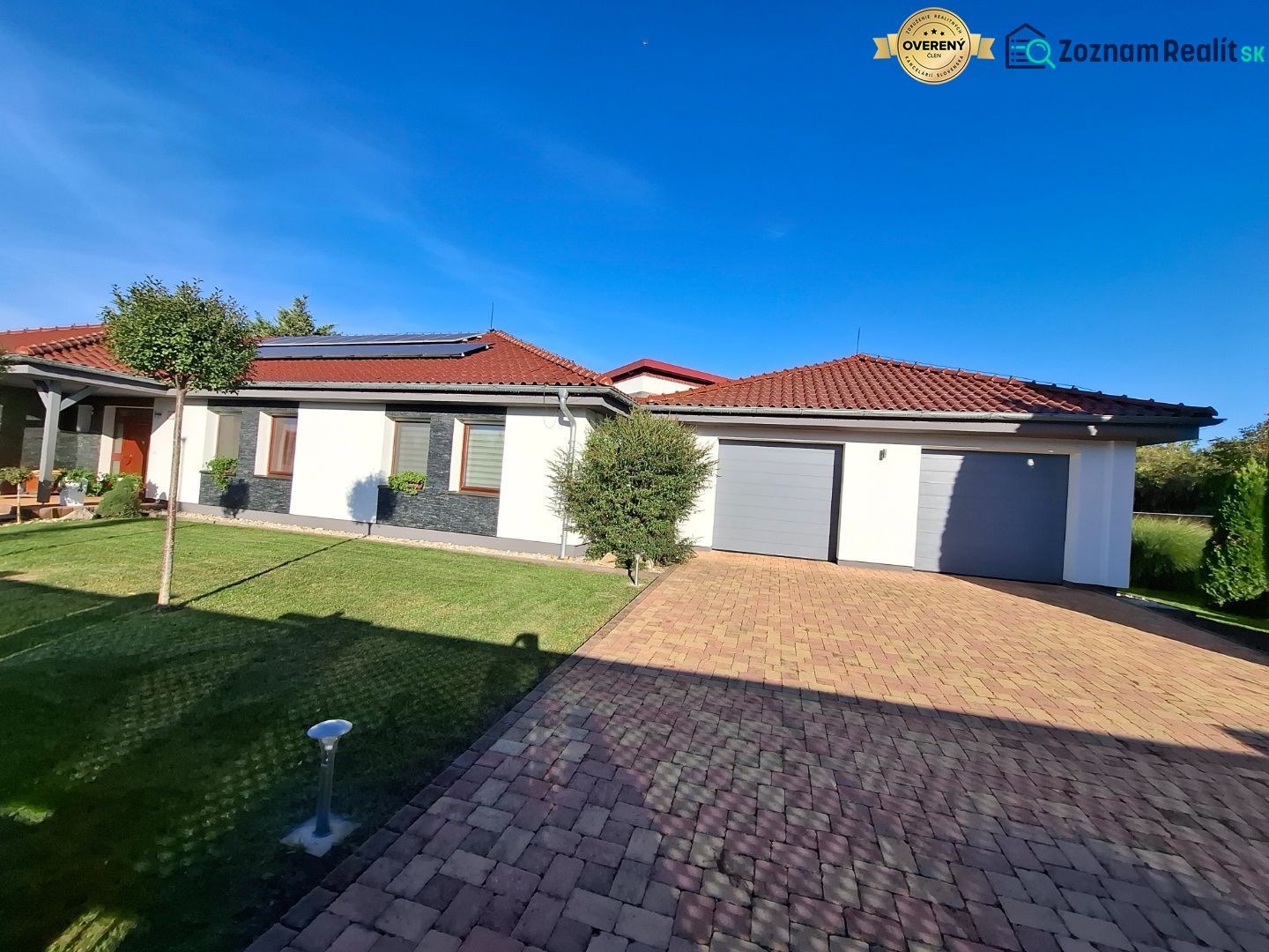 Ein Einfamilienhaus in Nové Zámky mit rotem Dach, Garage und gepflegtem Rasen.
