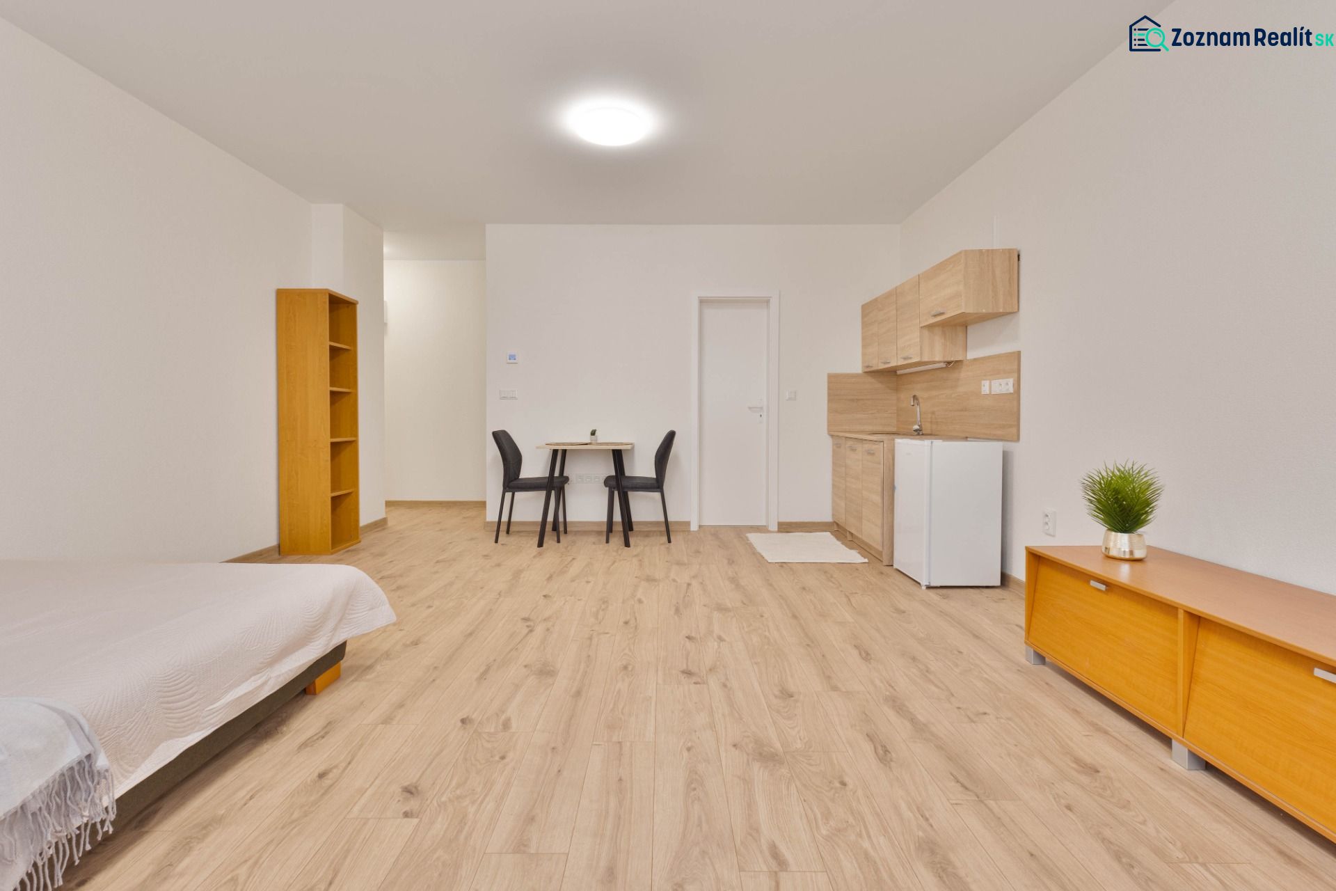 Einzimmerwohnung mit Küchenzeile, Möbeln und Bodenbelag in Holzoptik.