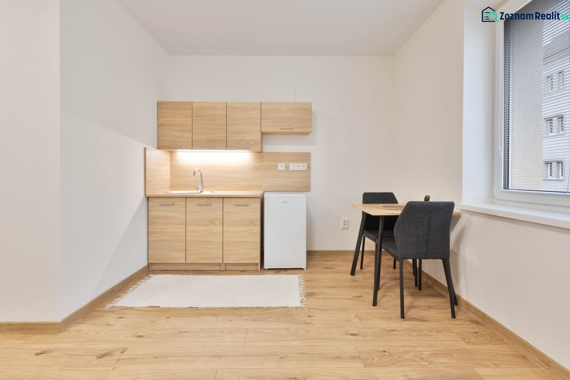 Einzimmerwohnung mit Küchenzeile, Kühlschrank und Tisch, ergänzt durch einen Boden mit Holzdekor.