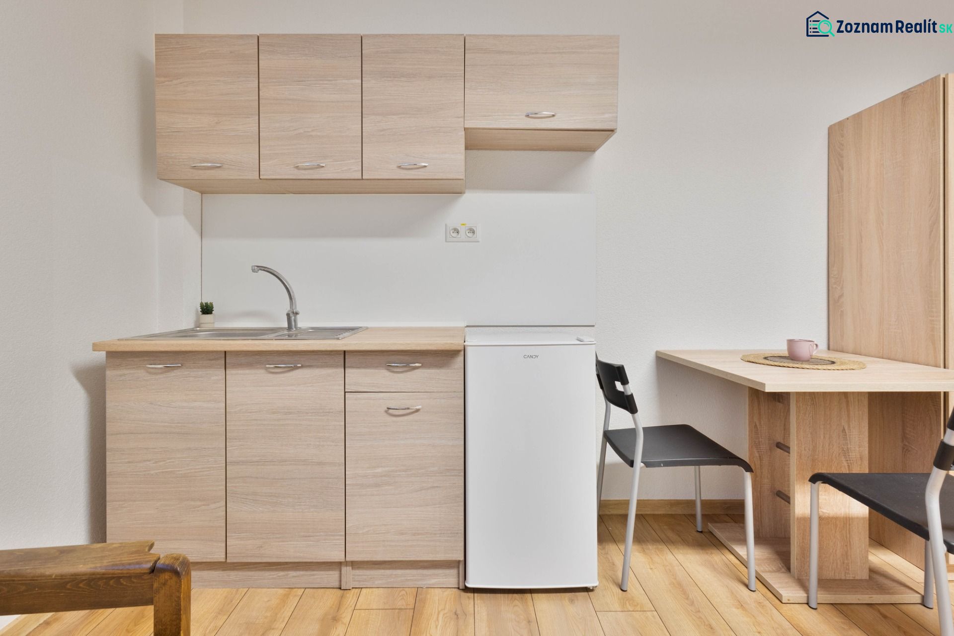 Küchenbereich in einem Einzimmerapartment mit weißem Kühlschrank und Holzboden.