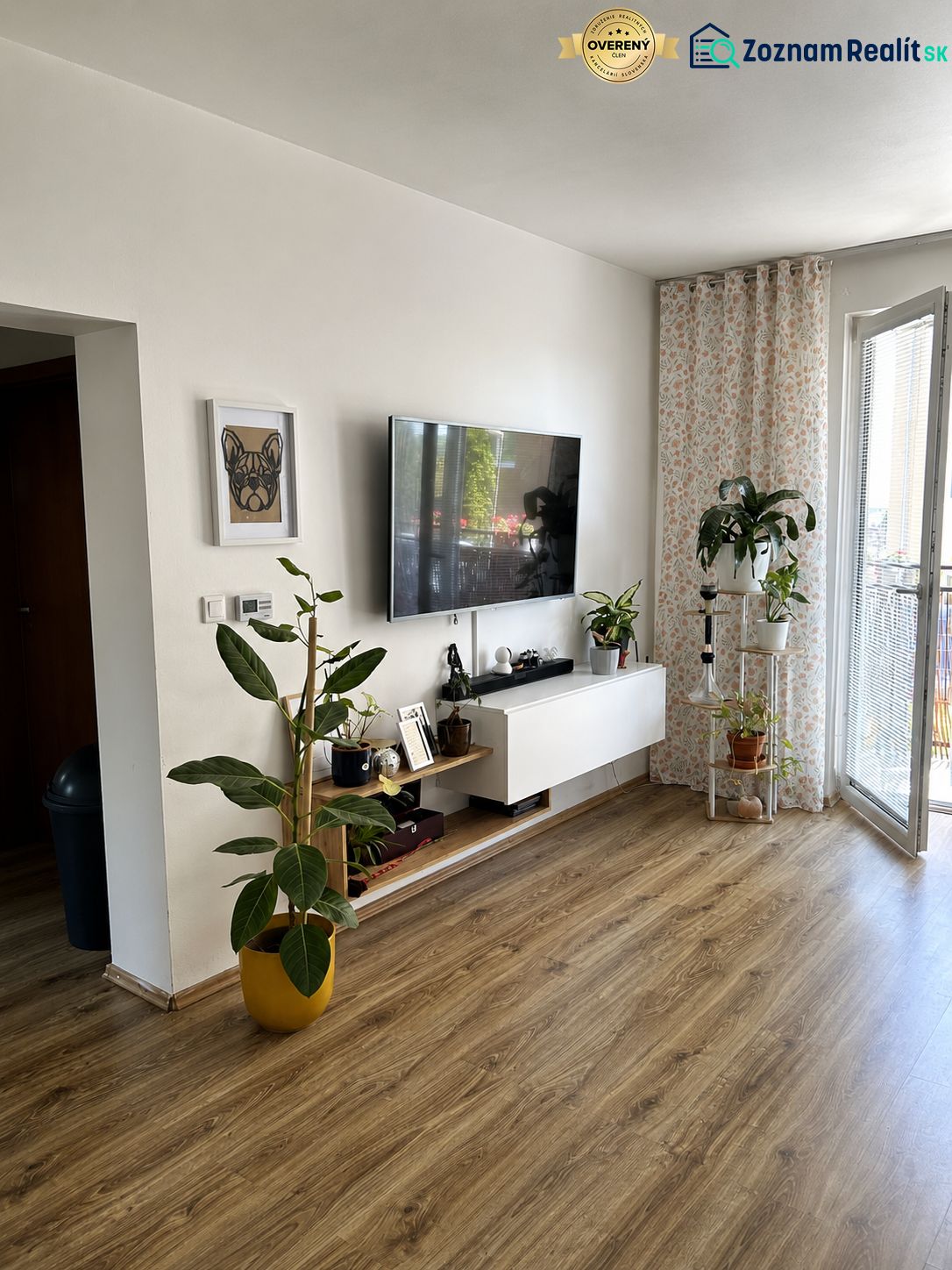 Ein Zimmer in einer 3-Zimmer-Wohnung mit einem Boden in Holzoptik, einem Fernseher und Pflanzen.