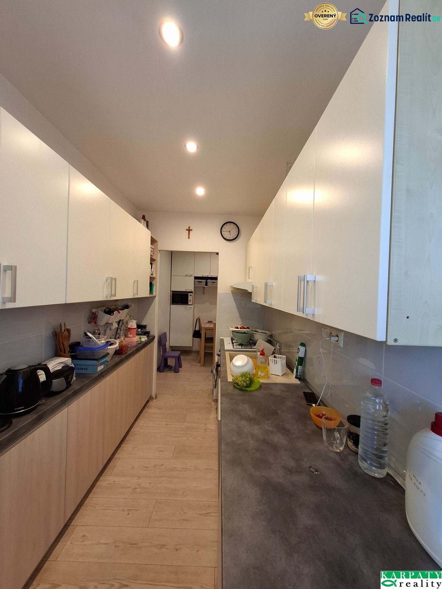 Küche in einer 3-Zimmer-Wohnung mit weißen Schränken und einem Boden in Holzoptik.