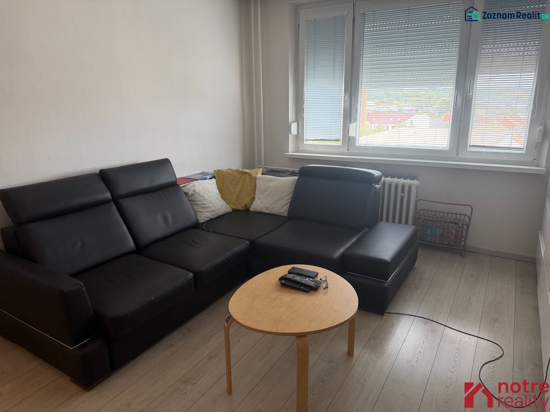 Wohnzimmer in einer 2-Zimmer-Wohnung mit schwarzem Sofa und Holzboden.