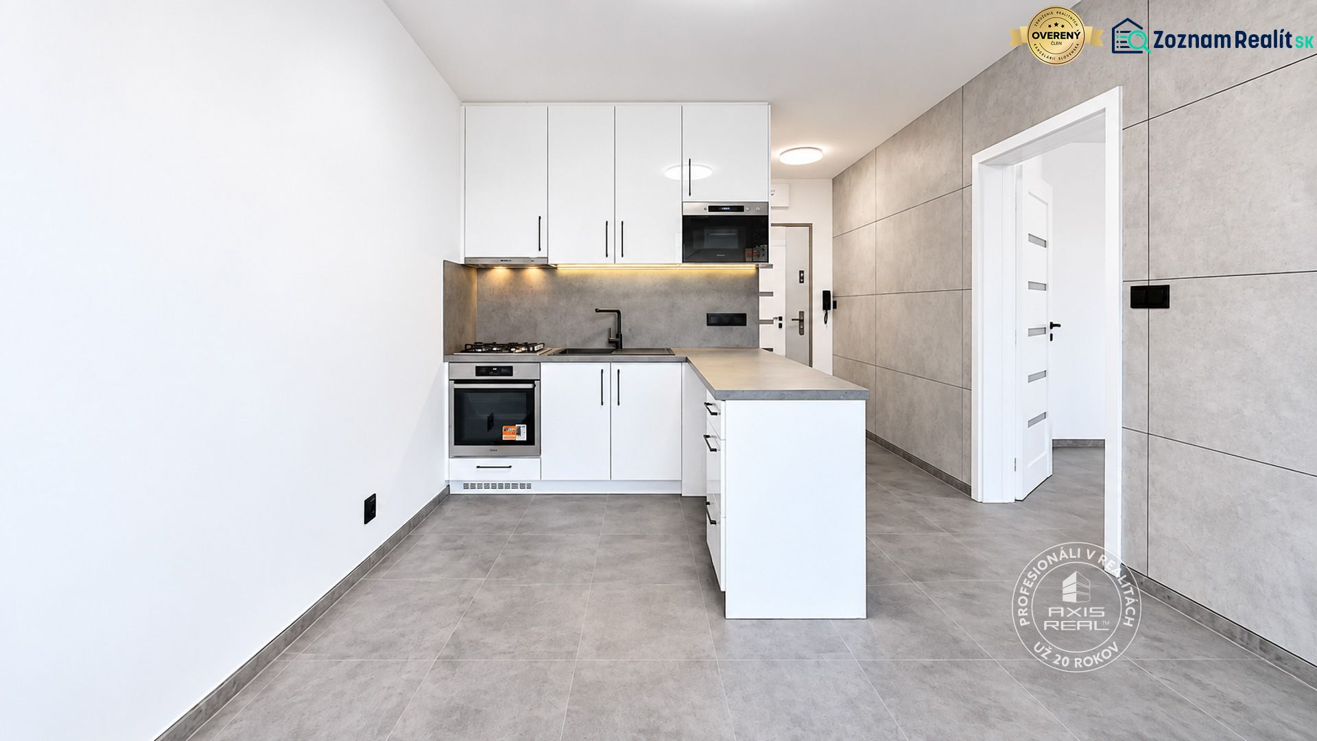Küche in einer 2-Zimmer-Wohnung mit weißen Schränken und grauen Fliesen.
