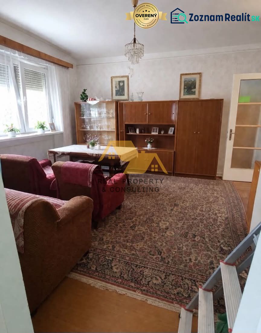 Wohnzimmer in einem Einfamilienhaus mit einer Sitzgarnitur, einem Schrank und einem Kronleuchter, Boden mit Holzdekor.
