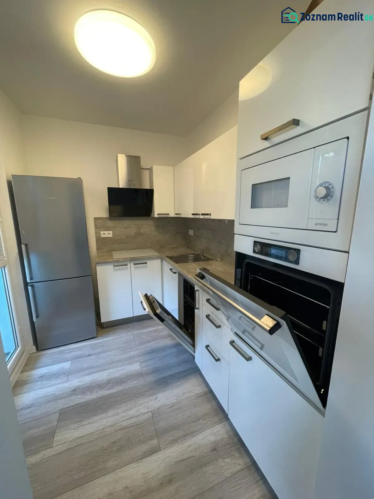Küche mit eingebautem Backofen, weißen Schränken und Holzboden in einer Zweizimmerwohnung.