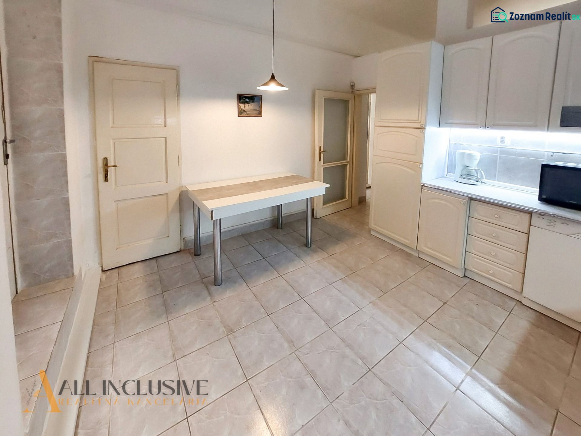 Küche in einer 2-Zimmer-Wohnung mit weißen Schränken, Tisch und Fliesen.