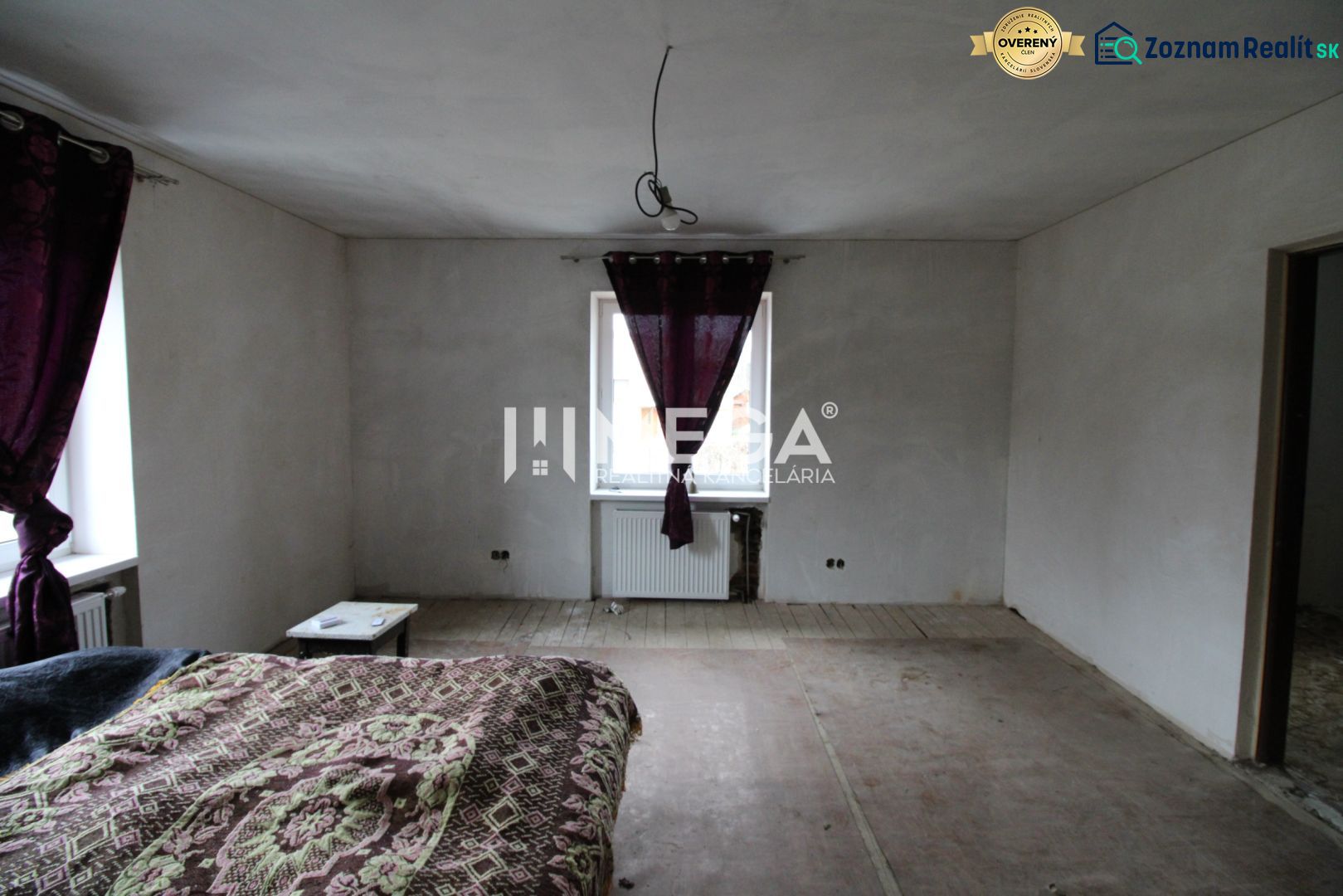 Schlafzimmer in einem Einfamilienhaus mit abblätterndem Boden und lila Vorhängen.