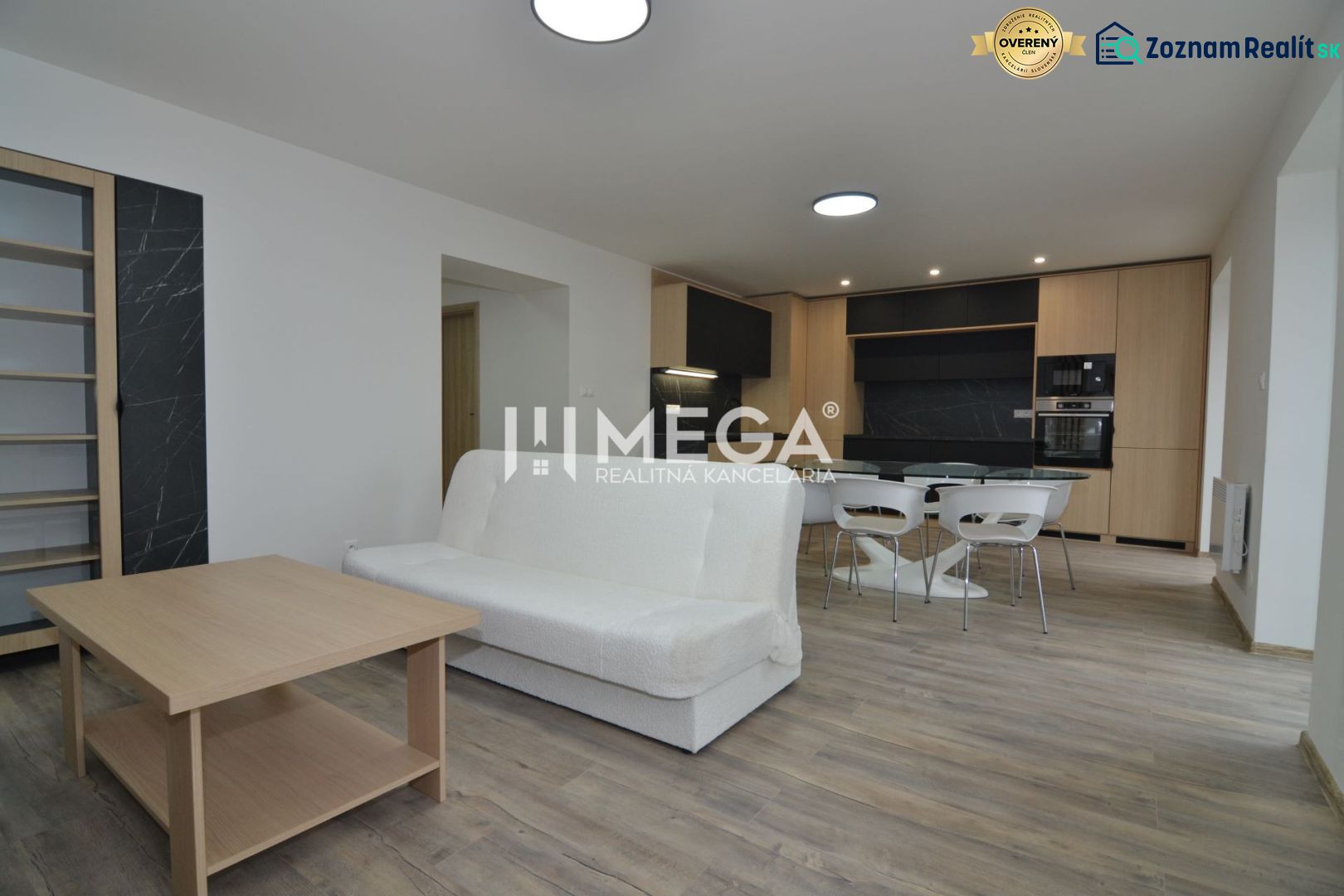Wohnzimmer in einer 3-Zimmer-Wohnung mit Holzboden und Küche im Hintergrund.
