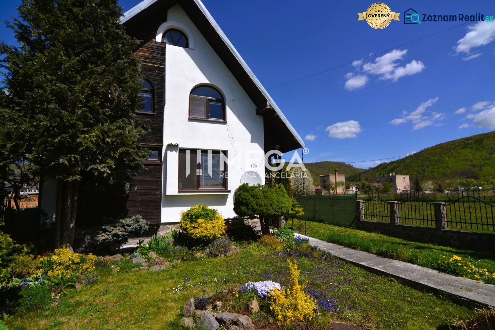 Ein Einfamilienhaus in Koškovce mit gepflegtem Garten und hügeligem Hintergrund unter blauem Himmel.