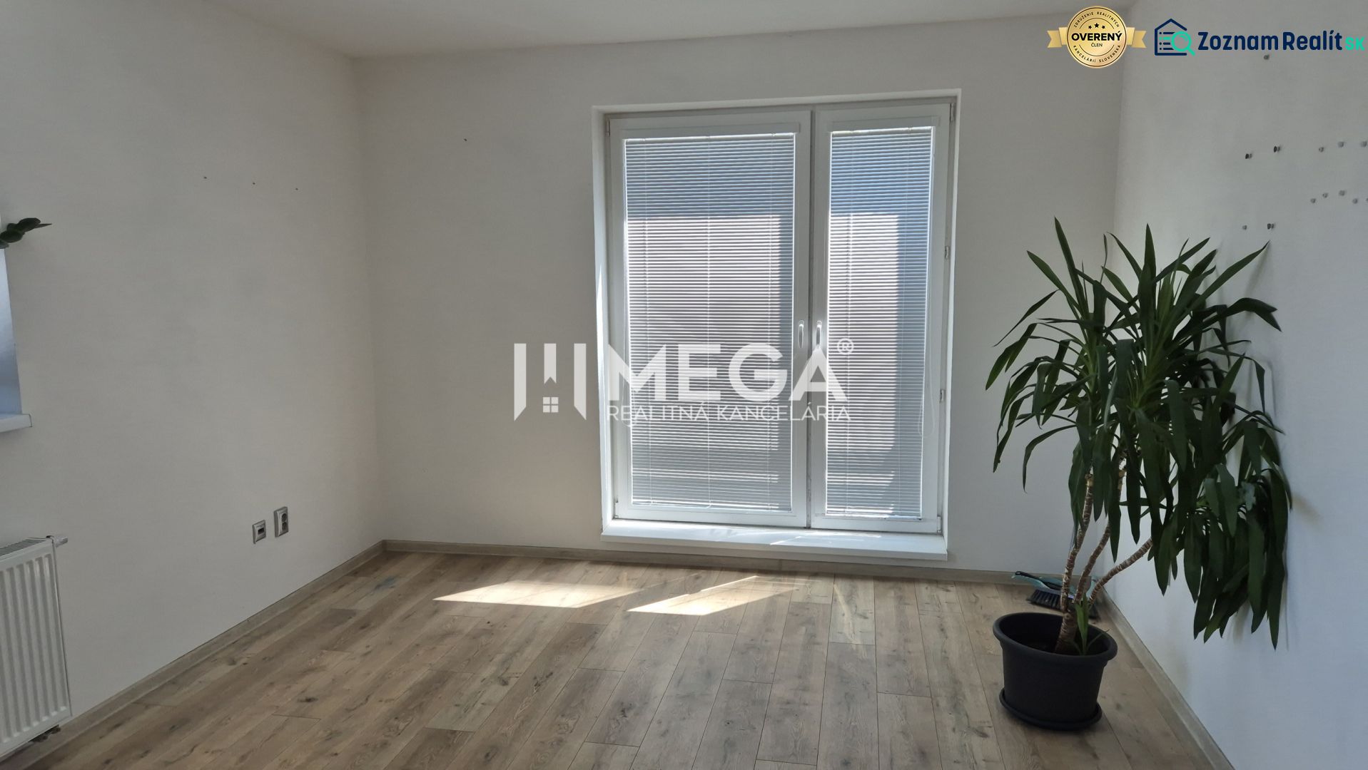 Ein Büro mit einer Pflanze, einem Holzboden und Balkontüren mit Jalousien.