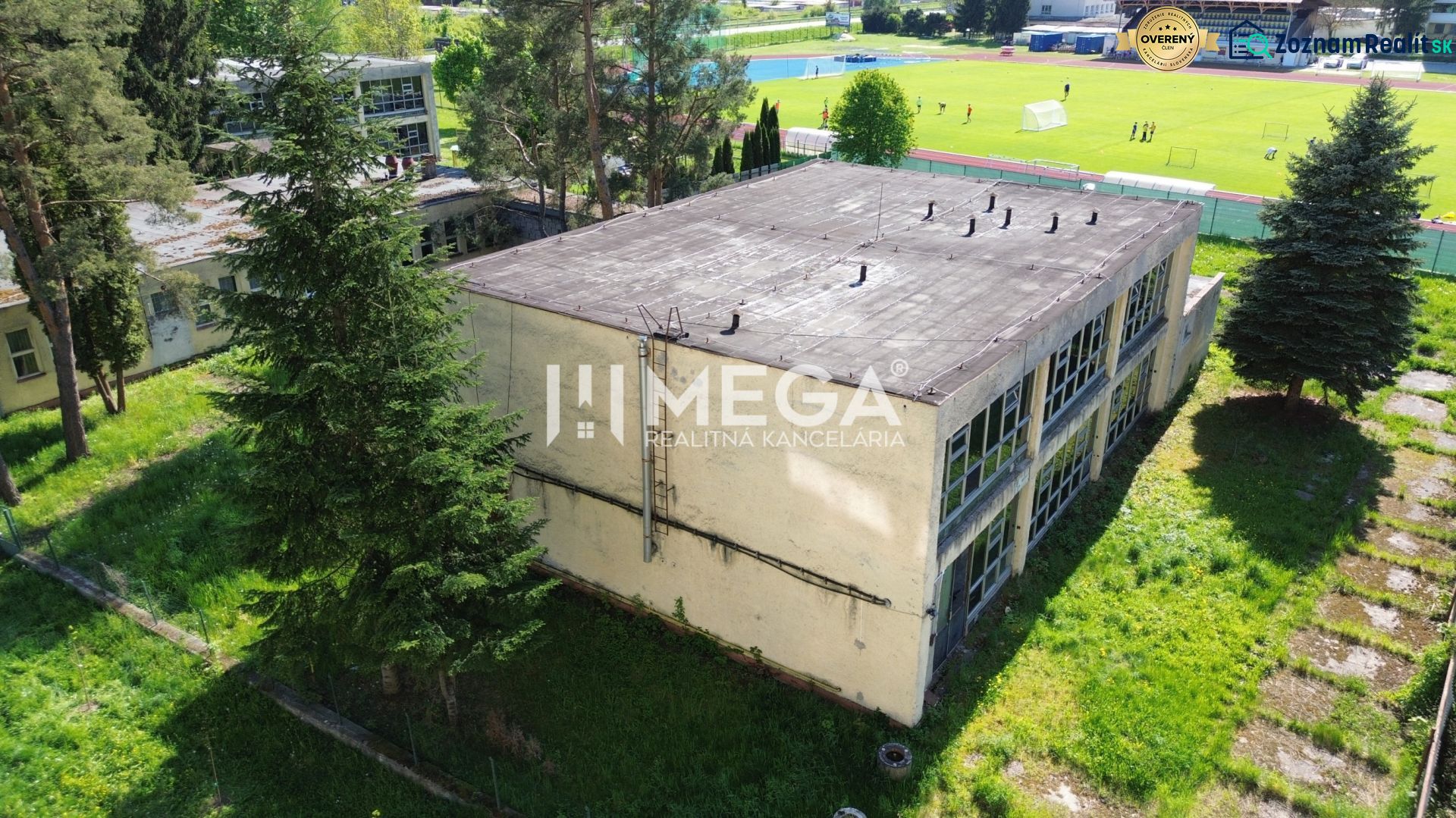 Das Gebäude in der Tyršova-Straße in Humenné, umgeben von Bäumen und einer Wiese mit einem Spielplatz im Hintergrund.