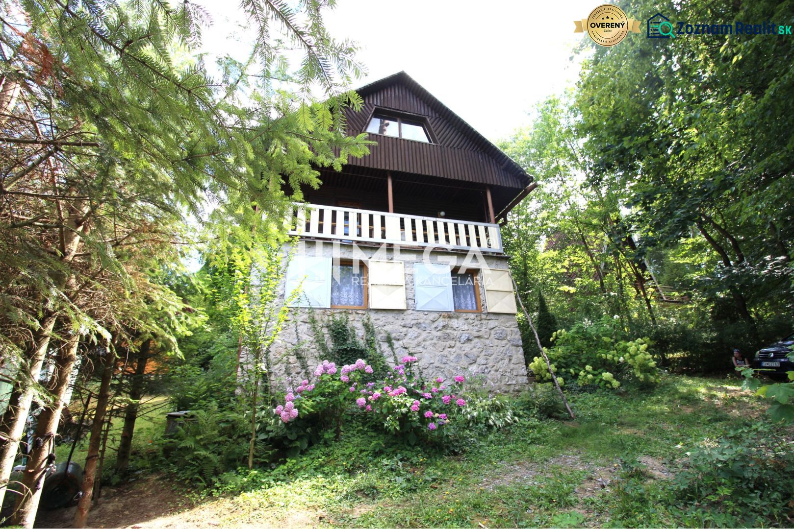 Eine Hütte in Holčíkovce, umgeben von Bäumen und Blumen, mit einem steinernen Unterteil.