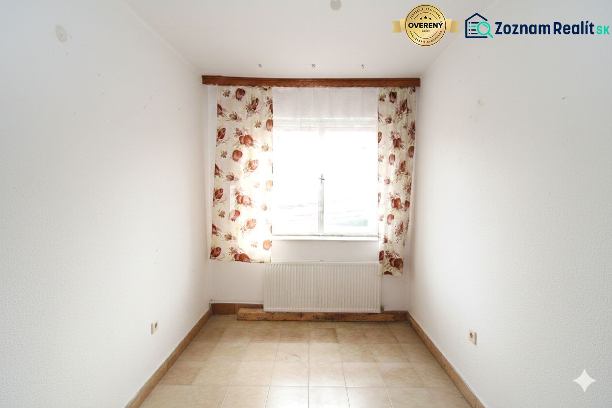 Ein Zimmer in einem Einfamilienhaus mit Fenster, Blumen-Vorhängen und Fliesen.