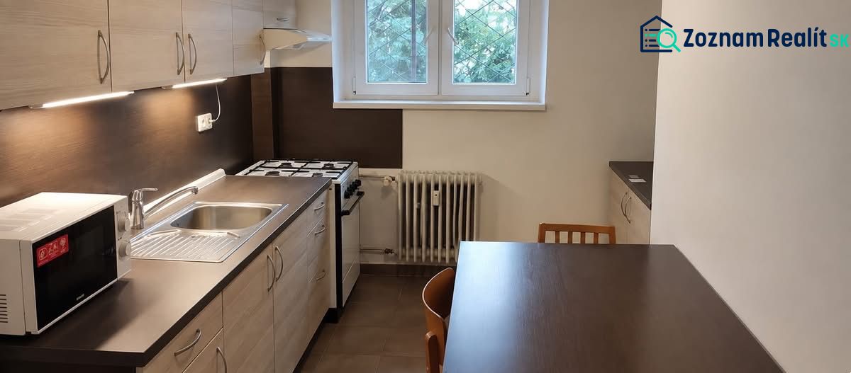Küche in einer Einzimmerwohnung mit Gasherd und Mikrowelle auf dunkler Küchenzeile.