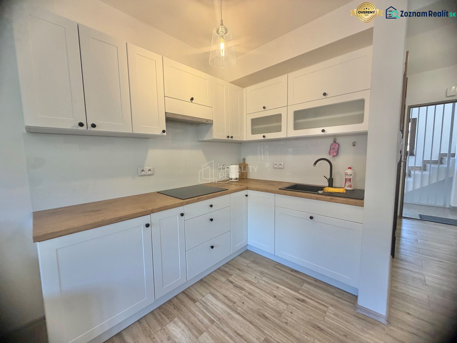 Küche in einer Einzimmerwohnung mit weißen Schränken und einem Boden in Holzoptik.
