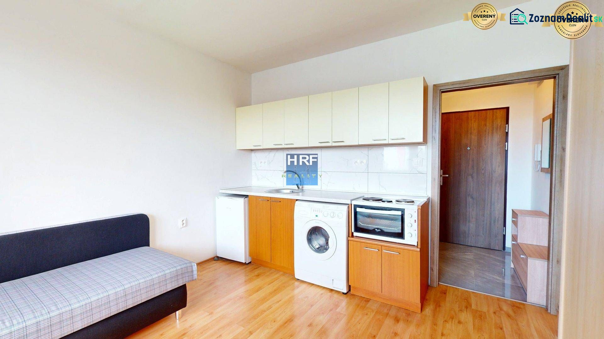 Küchenbereich eines Einzimmerapartments mit Sofa und Holzboden.