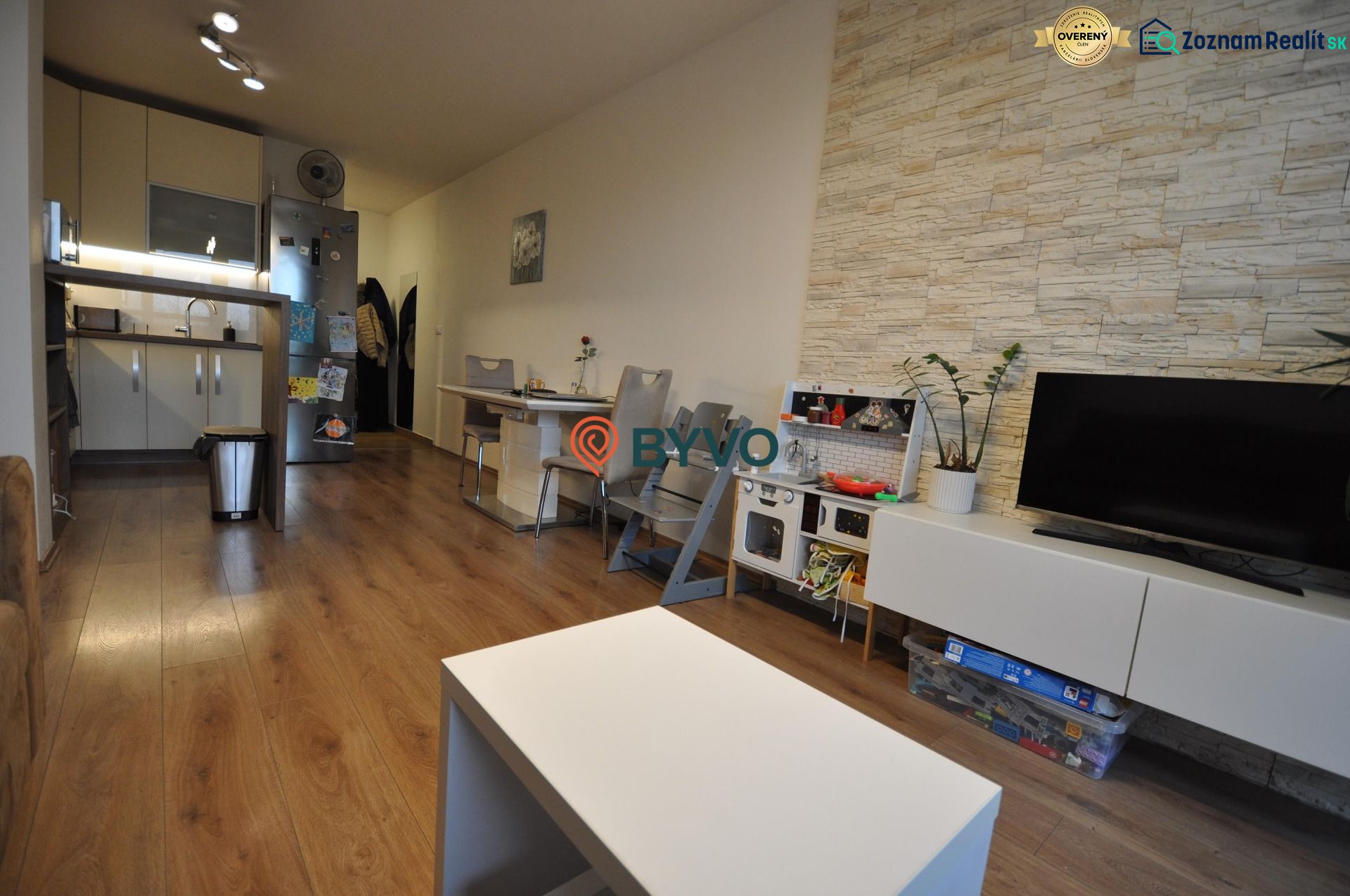 Wohnzimmer mit Holzboden, Küche, Esstisch und TV-Schrank.