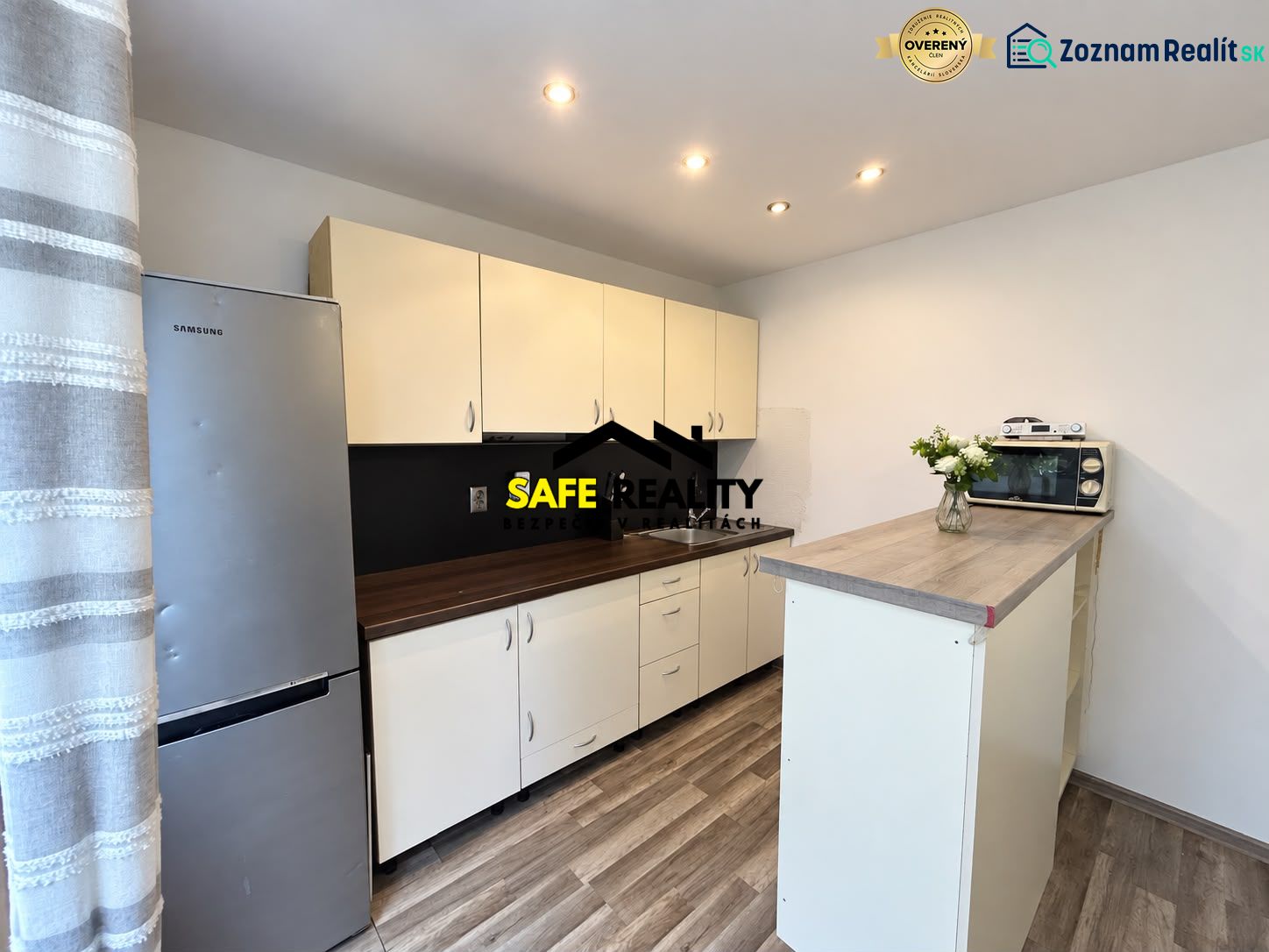 Küche mit Holzboden, hellen Schränken und Kühlschrank in einer Einzimmerwohnung.