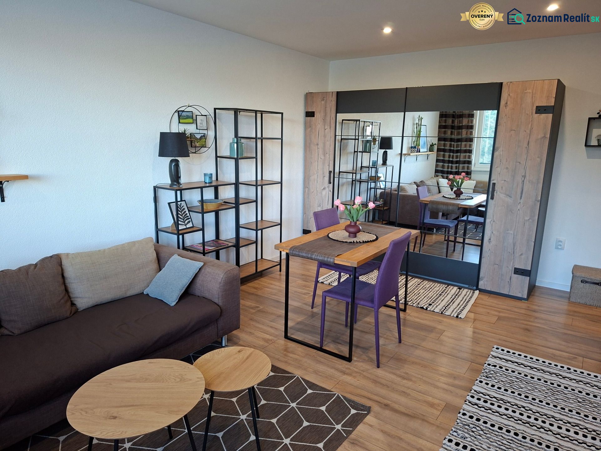 1-Zimmer-Wohnung mit Sofa, Esstisch und Bodenbelag in Holzoptik.
