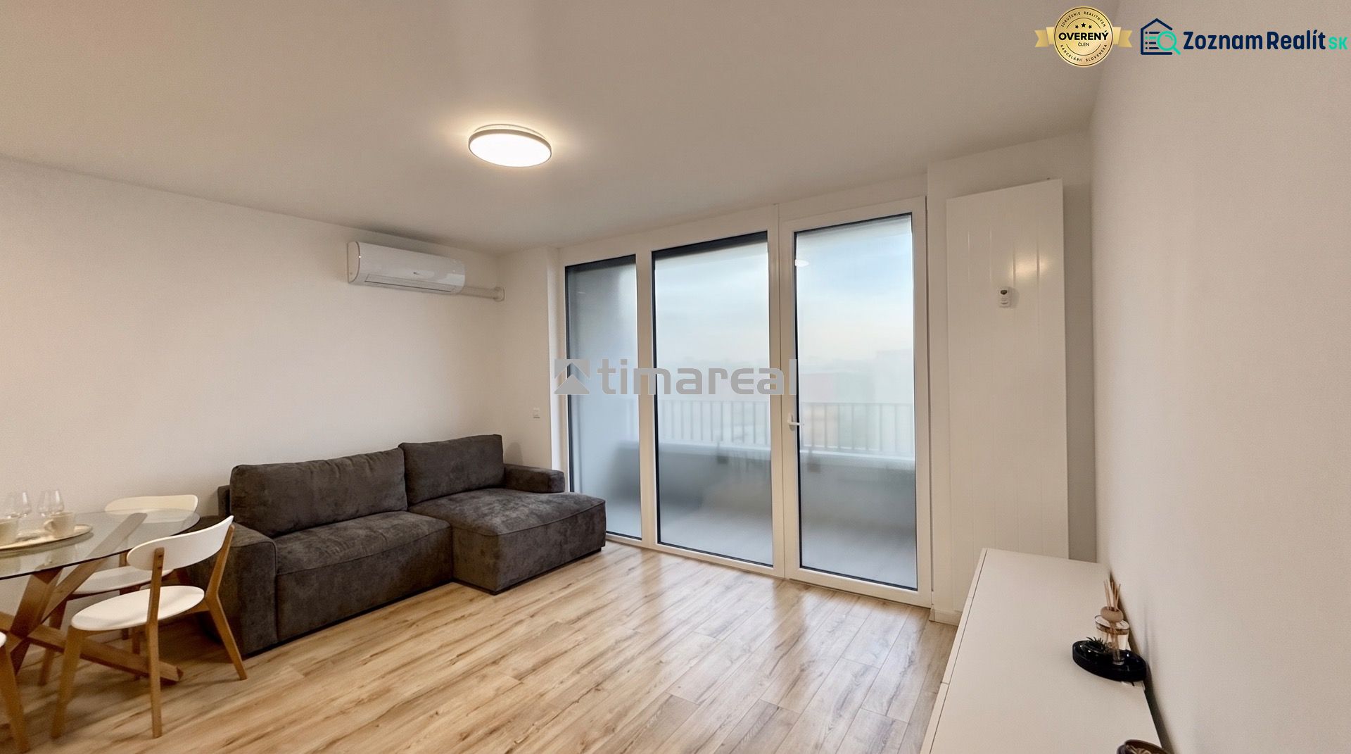 Wohnzimmer in einer Zweizimmerwohnung mit Holzboden, grauem Sofa, Glastisch.