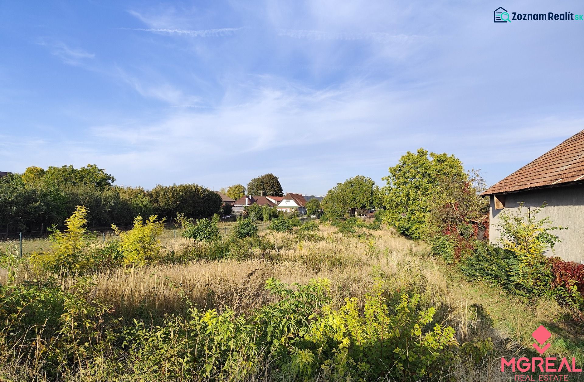 Grundstücke - Wohnen in Jasová, umgeben von Grün mit sichtbaren Gebäuden im Hintergrund.