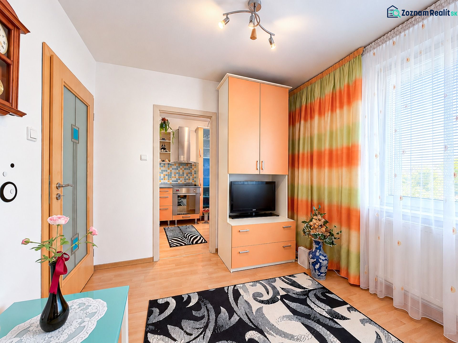 Eine Einzimmerwohnung mit hellen Wänden, orangefarbenen Möbeln und dekorativen Vorhängen.