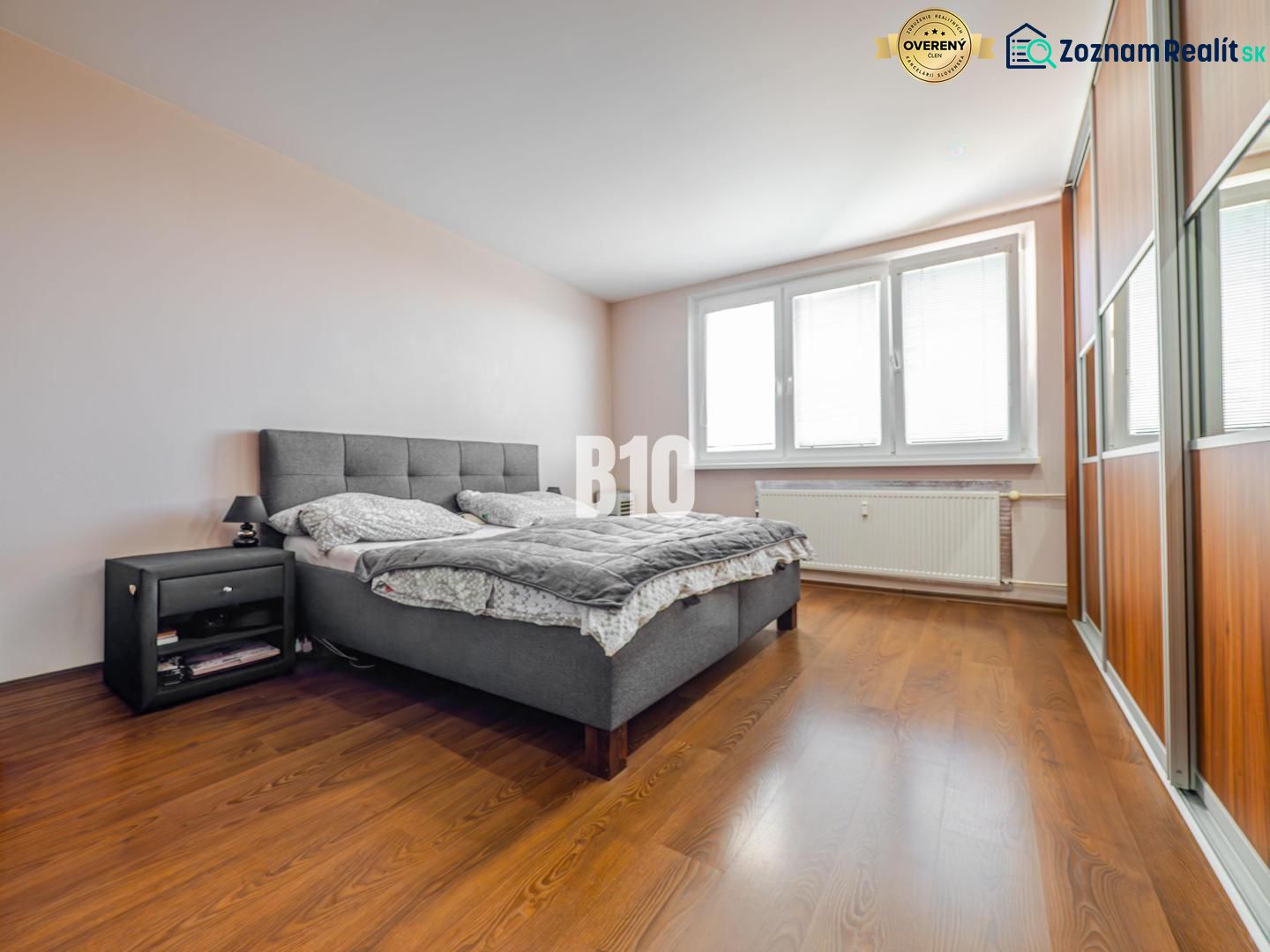 Schlafzimmer mit großem Bett, Nachttisch und Boden mit Holzdekor in einer 3-Zimmer-Wohnung.