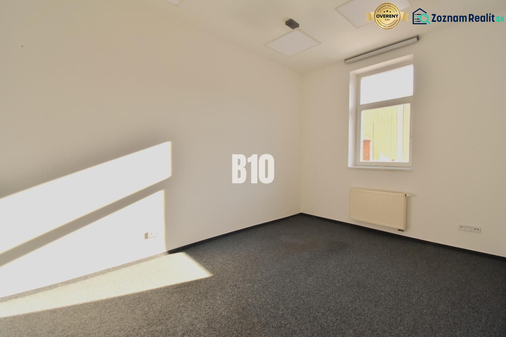 Büroinnenraum mit Teppichboden und Fenster, Blick auf eine Wand und Heizkörper.