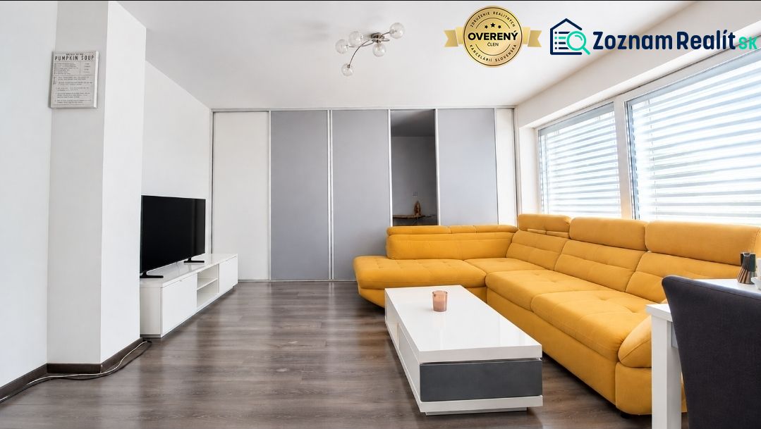 Wohnzimmer in einem Einfamilienhaus mit gelbem Sofa, Fernseher und Holzboden.