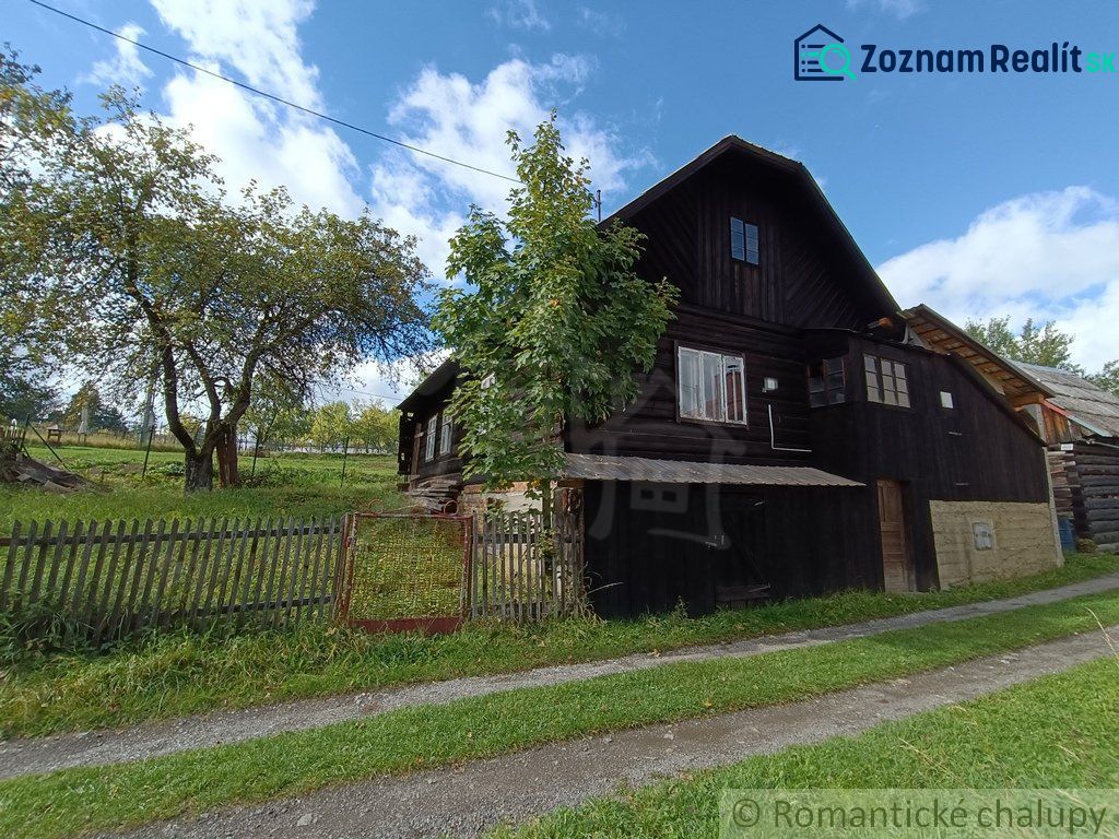 Eine Holzhütte in Staškov, umgeben von Bäumen und einem Zaun auf einer geräumigen grünen Fläche.