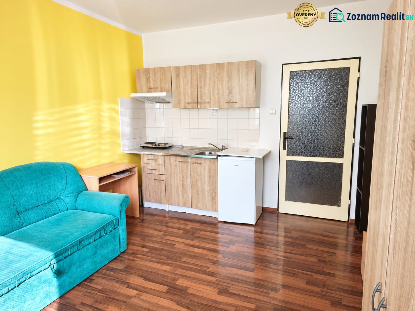 Einzimmerwohnung mit gelber Wand, Küchenzeile und Sofa, Boden mit Holzdekor.
